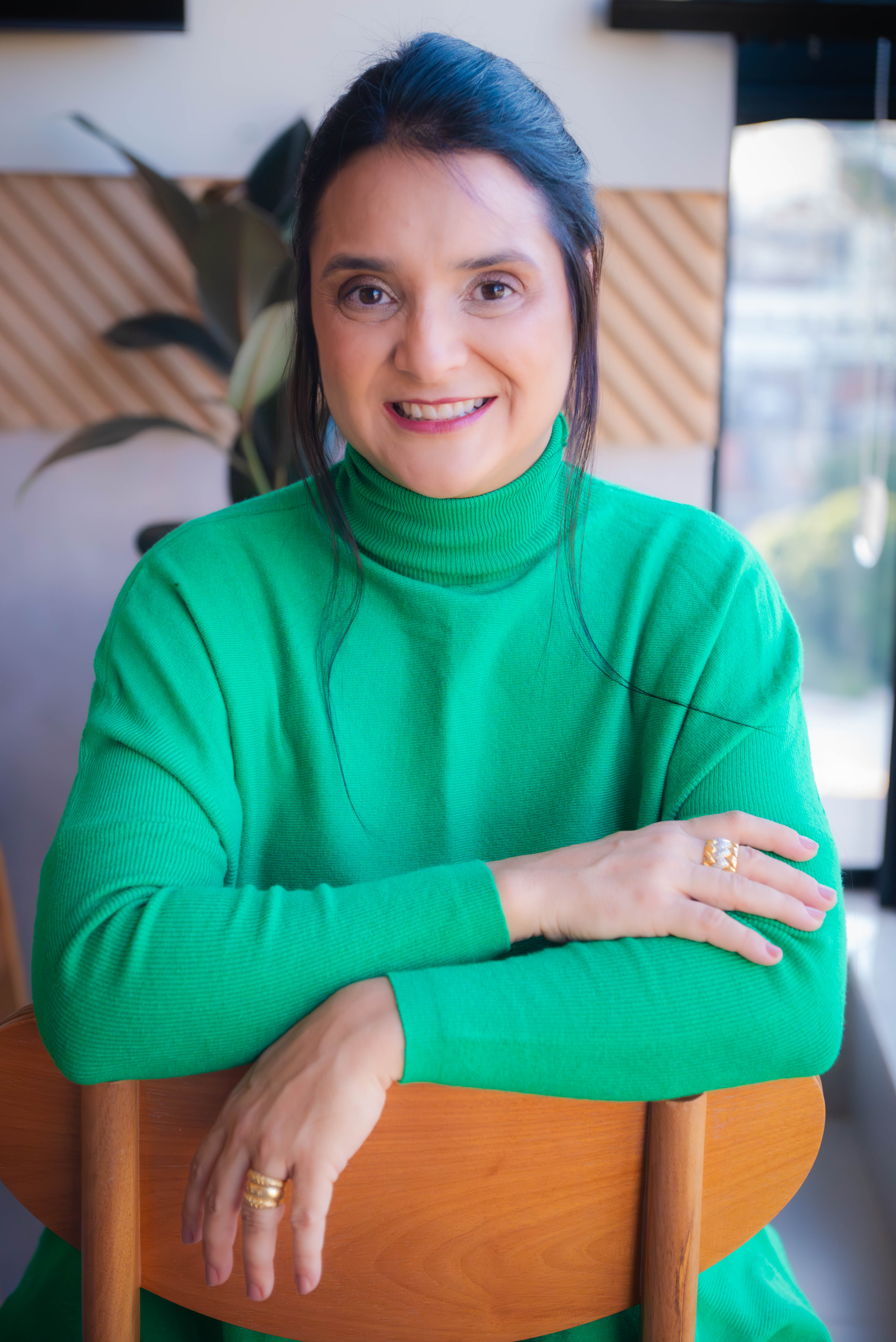 Juliana Monteiro sorrindo, com malha verde, em ambiente acolhedor.